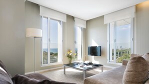 Una sala de estar moderna con un sofá, una mesa de centro y un televisor. Amplios ventanales ofrecen vistas al exterior.
