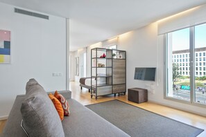 Una sala de estar moderna con un sofá gris, un tapete pequeño, una estantería de madera y un televisor.
