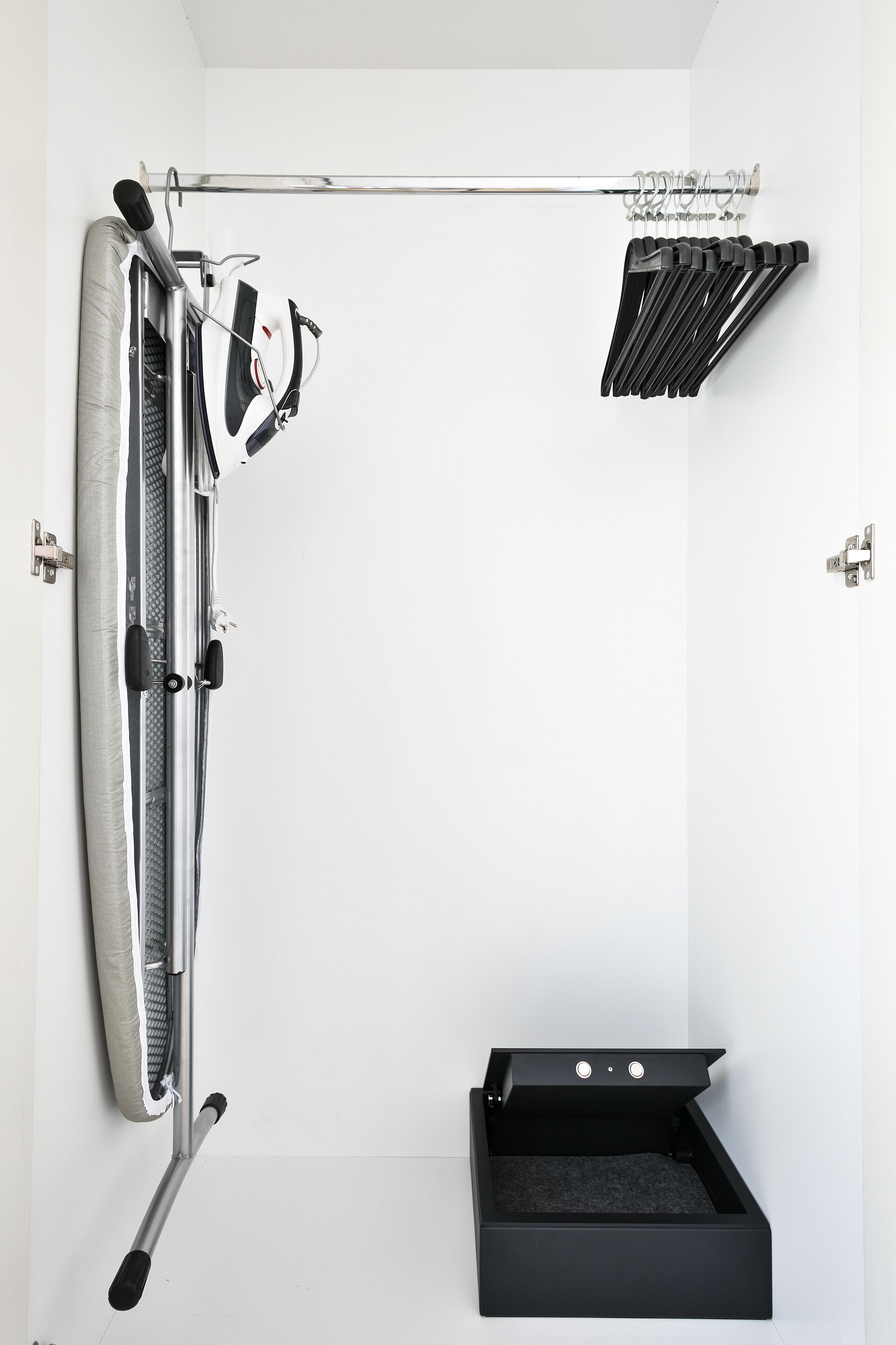 Een kleine kamer met een aan de muur bevestigde hometrainer, een kledingrek en een zwarte opbergdoos.