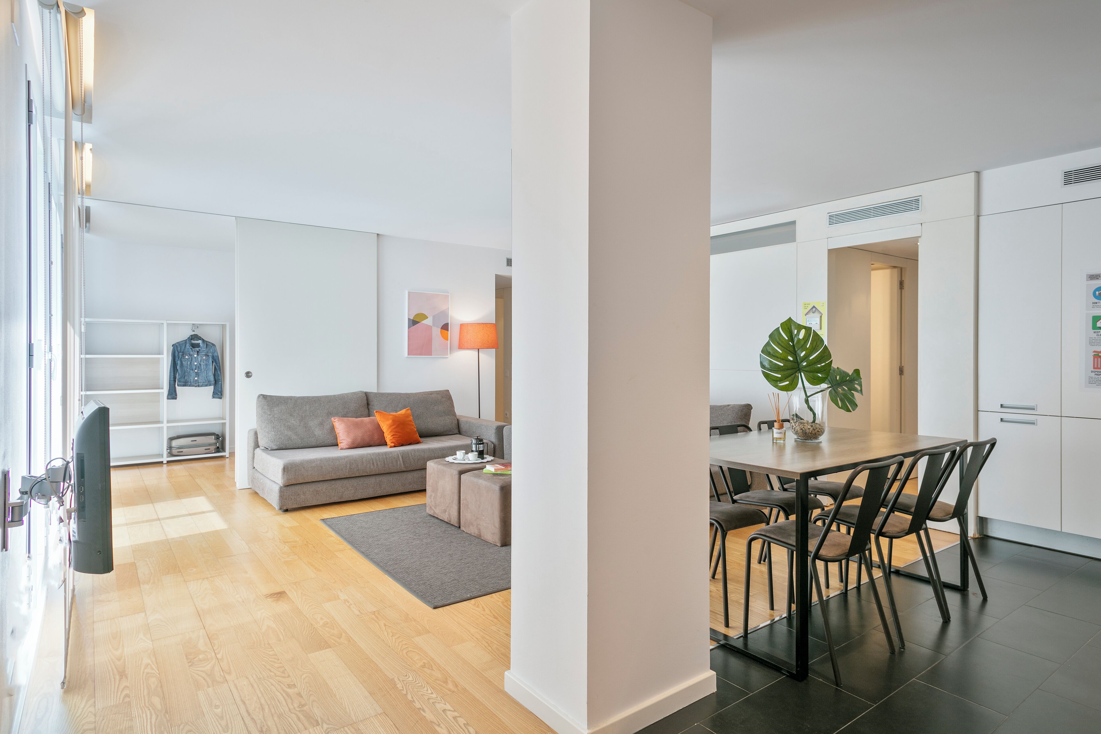 A modern living room with a grey sofa, a coffee table, and a dining area with a wooden table and chairs.