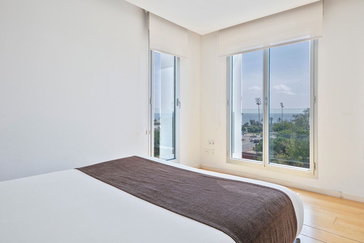 A modern bedroom with a large bed, a view of the city through floor-to-ceiling windows, and a minimalist design.
