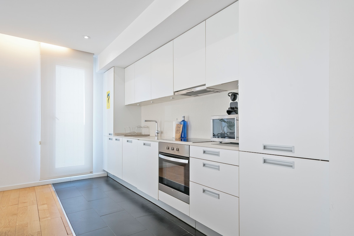 A modern kitchen with white cabinetry, a built-in oven, and a large window.