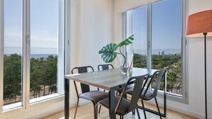 Un comedor con una mesa grande y sillas, ventanas amplias que ofrecen vistas de la ciudad, y una planta en maceta sobre la mesa.