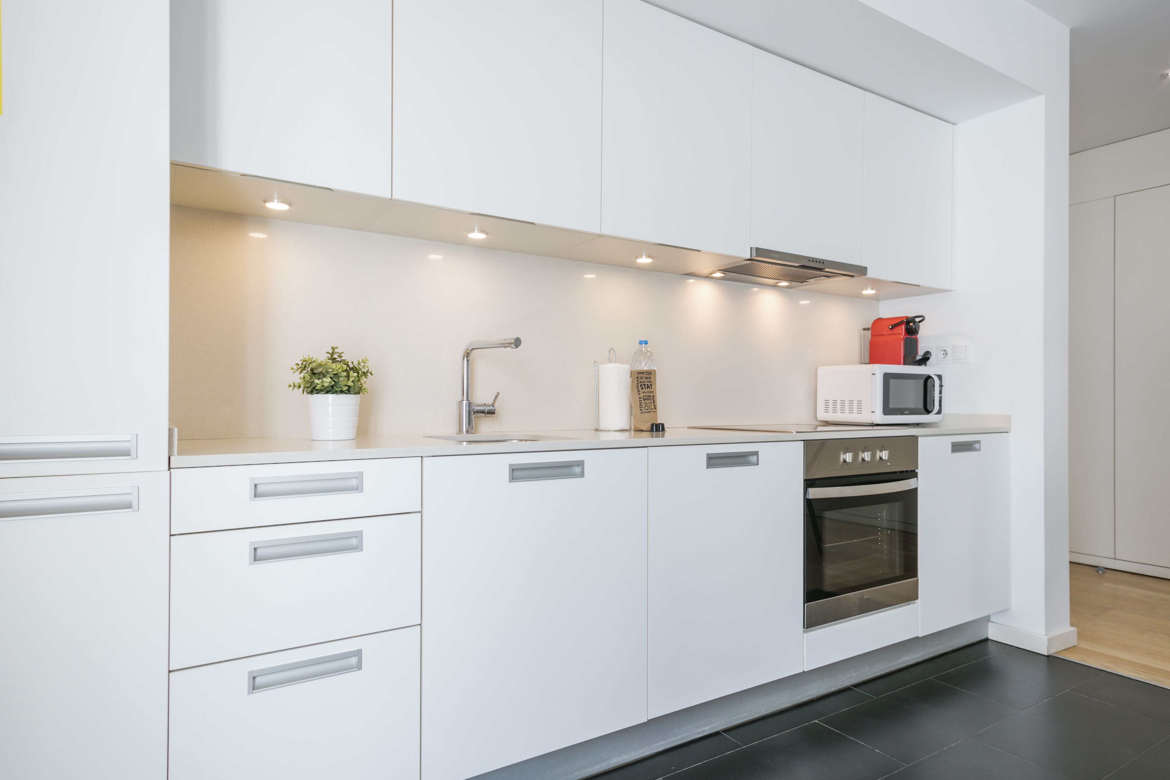 Eine moderne Küche mit weißen Schränken, einem Edelstahlbackofen, einer Mikrowelle und einem Spülbecken.