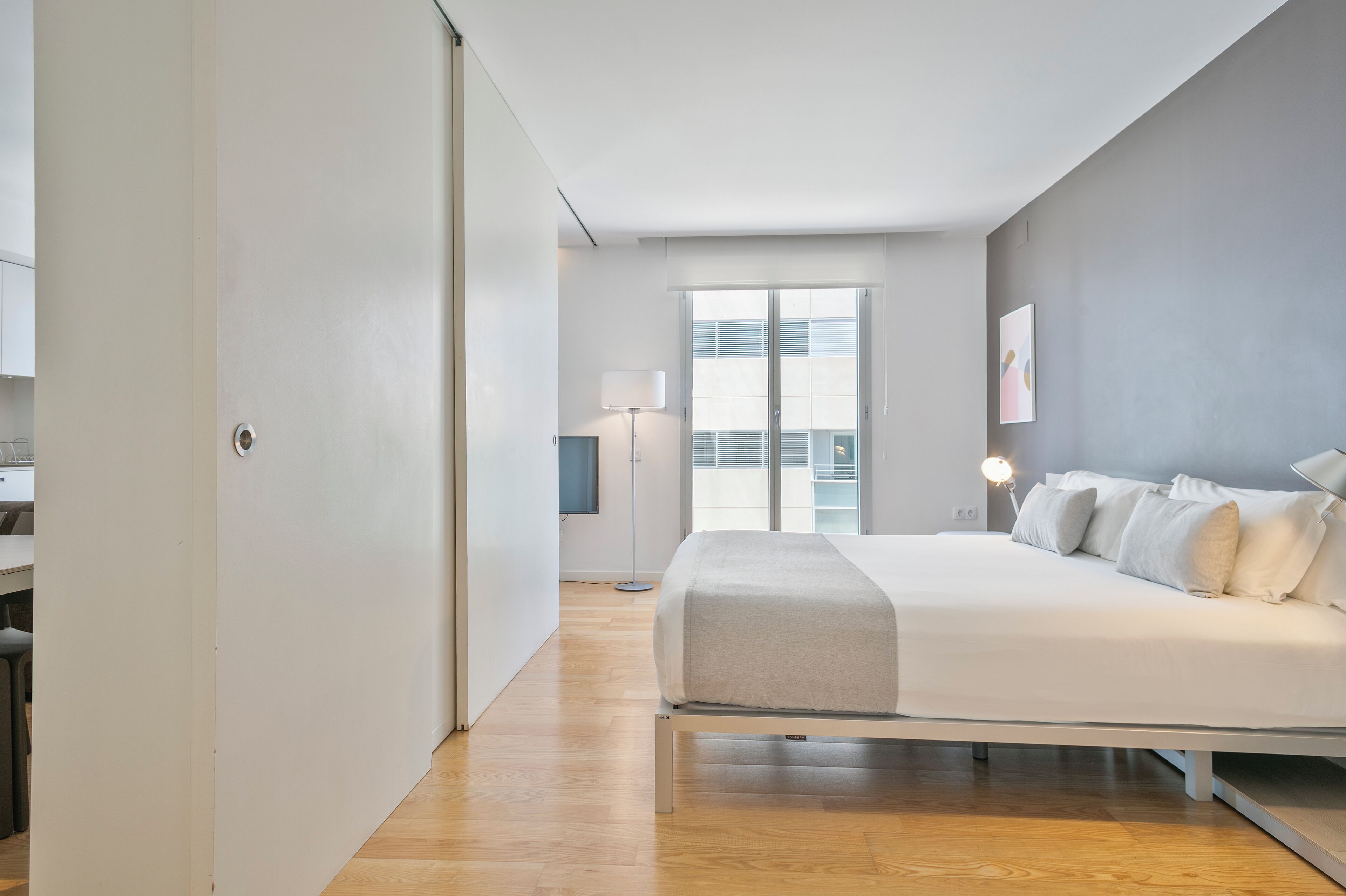 A modern bedroom with a large bed, a TV, and a balcony with a view.