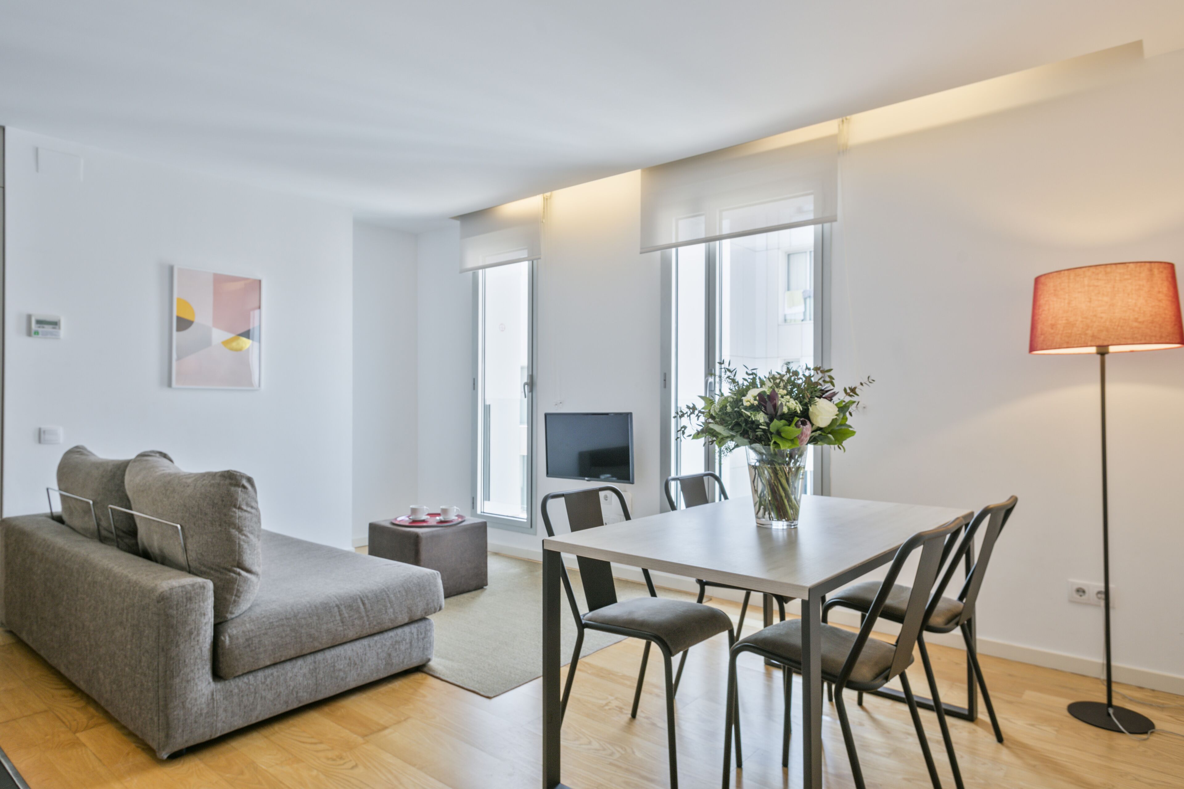 Una sala de estar moderna con un sofá gris, una mesa de comedor con sillas, un televisor y una lámpara de pie.