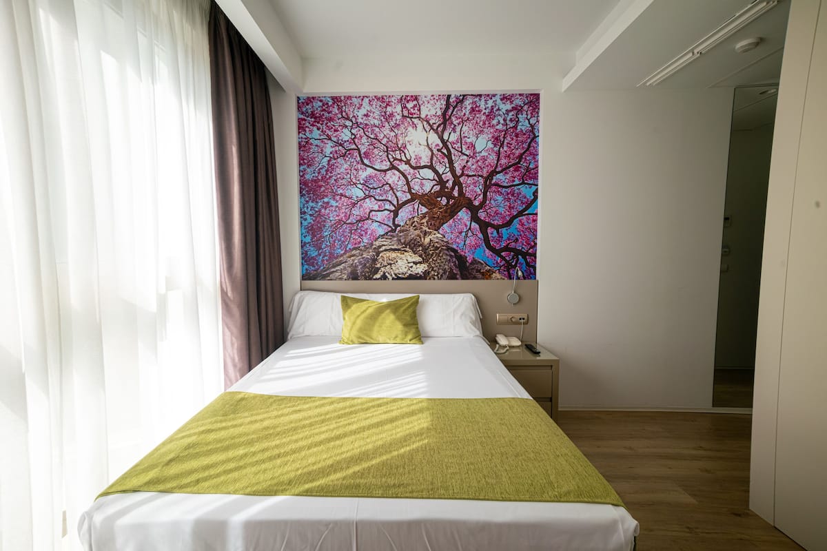 A hotel room with a bed, a nightstand, a telephone, and a painting of a tree.