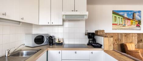 Una cocina moderna con armarios blancos, microondas integrado y cafetera.