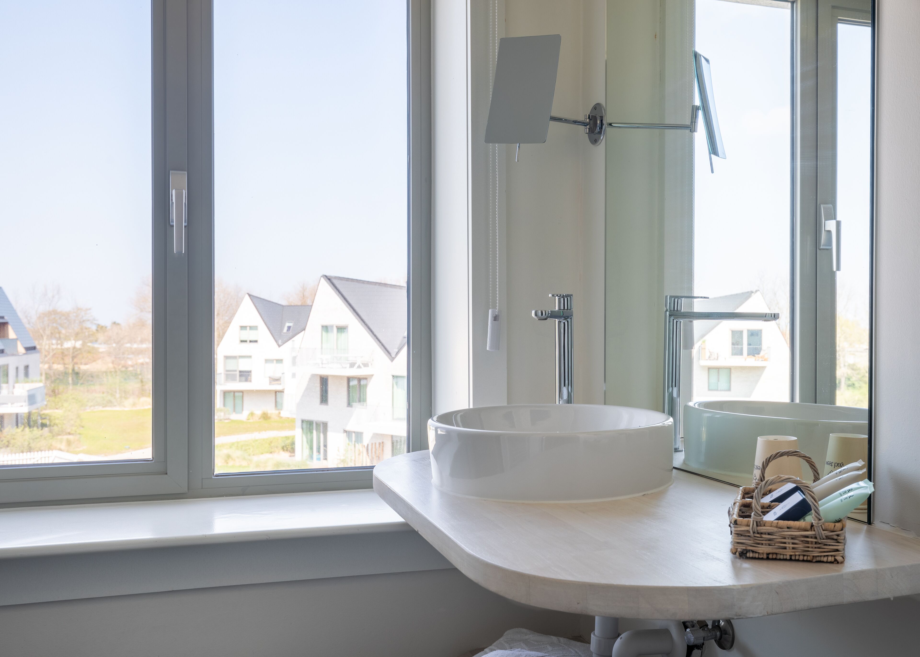 A bathroom with a large window, a white sink, and a mirror.