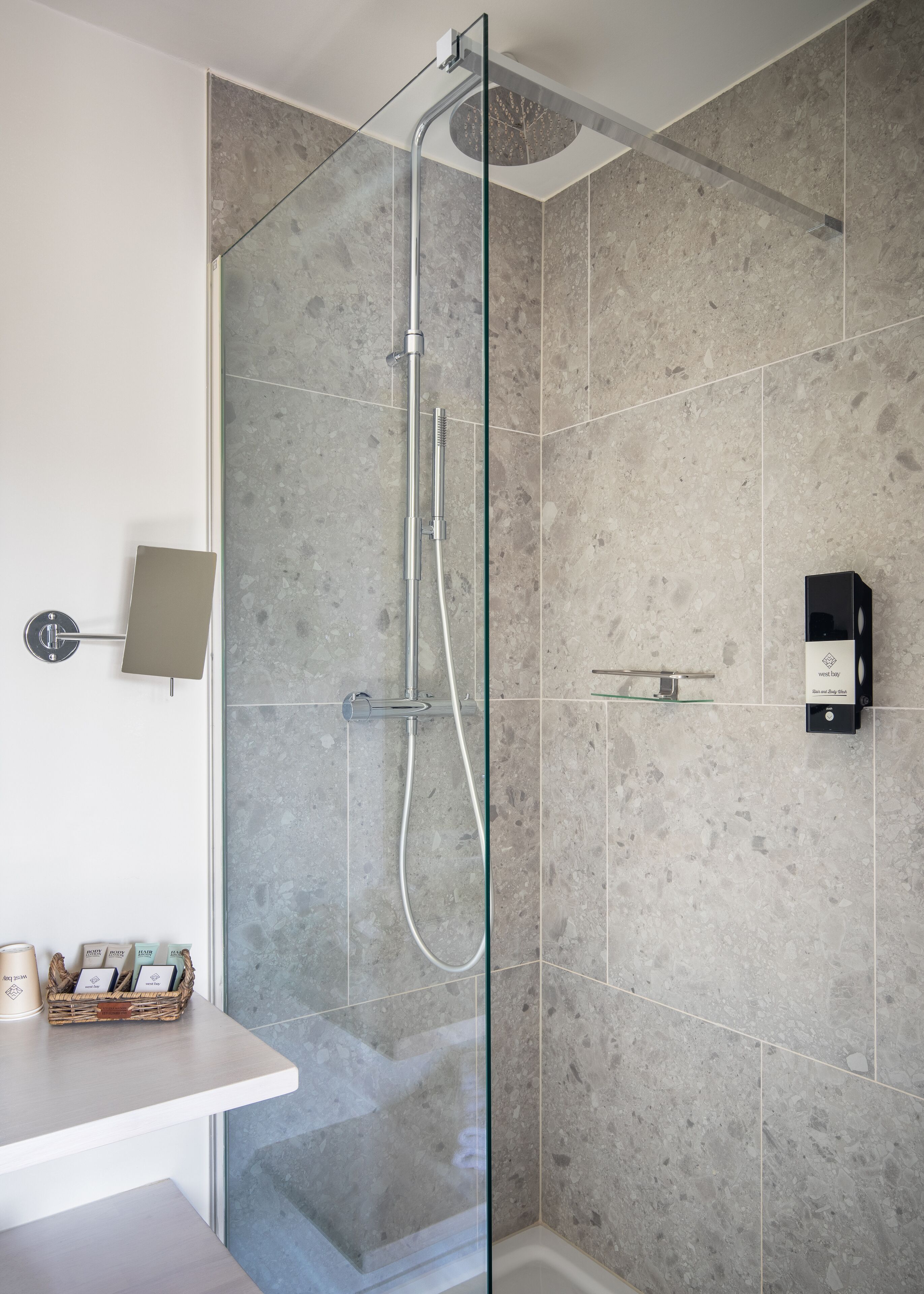 A modern bathroom with a glass-enclosed shower, a white countertop, and a wall-mounted soap dispenser.