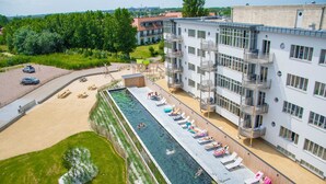 A swimming pool adjacent to a multi-story building with balconies and a parking area. - West Bay (Middelkerke)