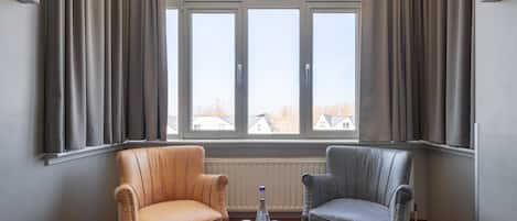 A room with two leather armchairs, a wooden coffee table with water bottles, and a large window with curtains.