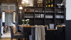 A modern bar area with wooden flooring, black bar stools, and a black shelving unit with glassware and bottles. - West Bay (Middelkerke)