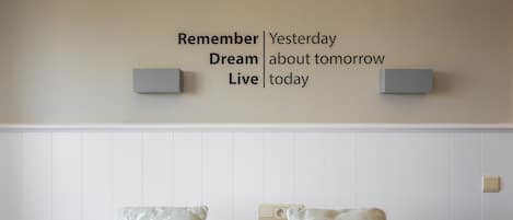 A neatly made bed with two pillows, a wall with motivational text, and a power outlet.