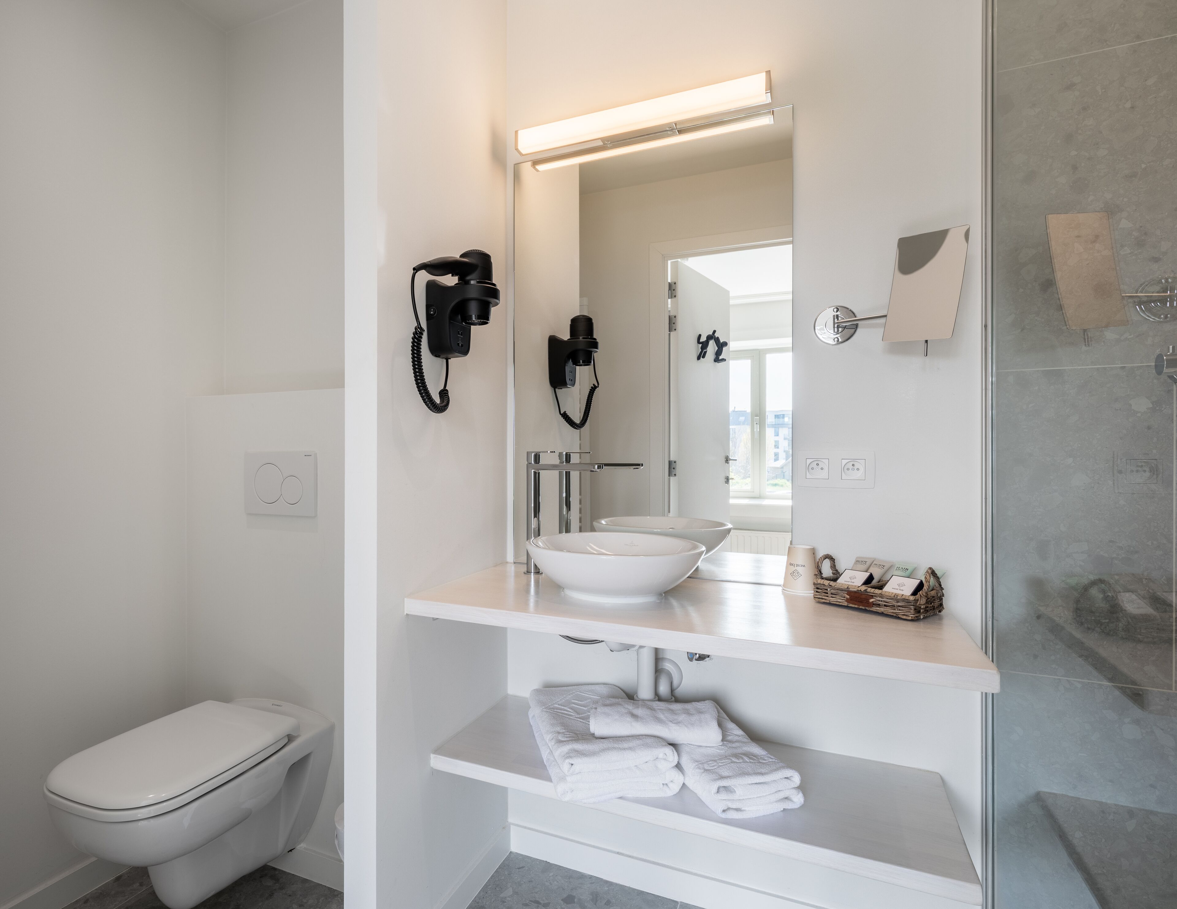 Ein modernes Badezimmer mit Toilette, Waschbecken mit Spiegel darüber und Duschbereich.