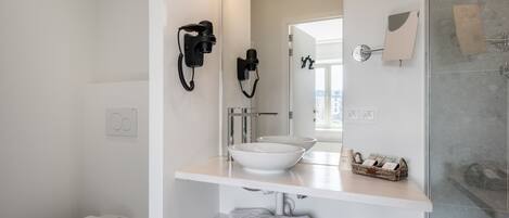 Un baño moderno con inodoro blanco, un lavabo con espejo superior y zona de ducha.