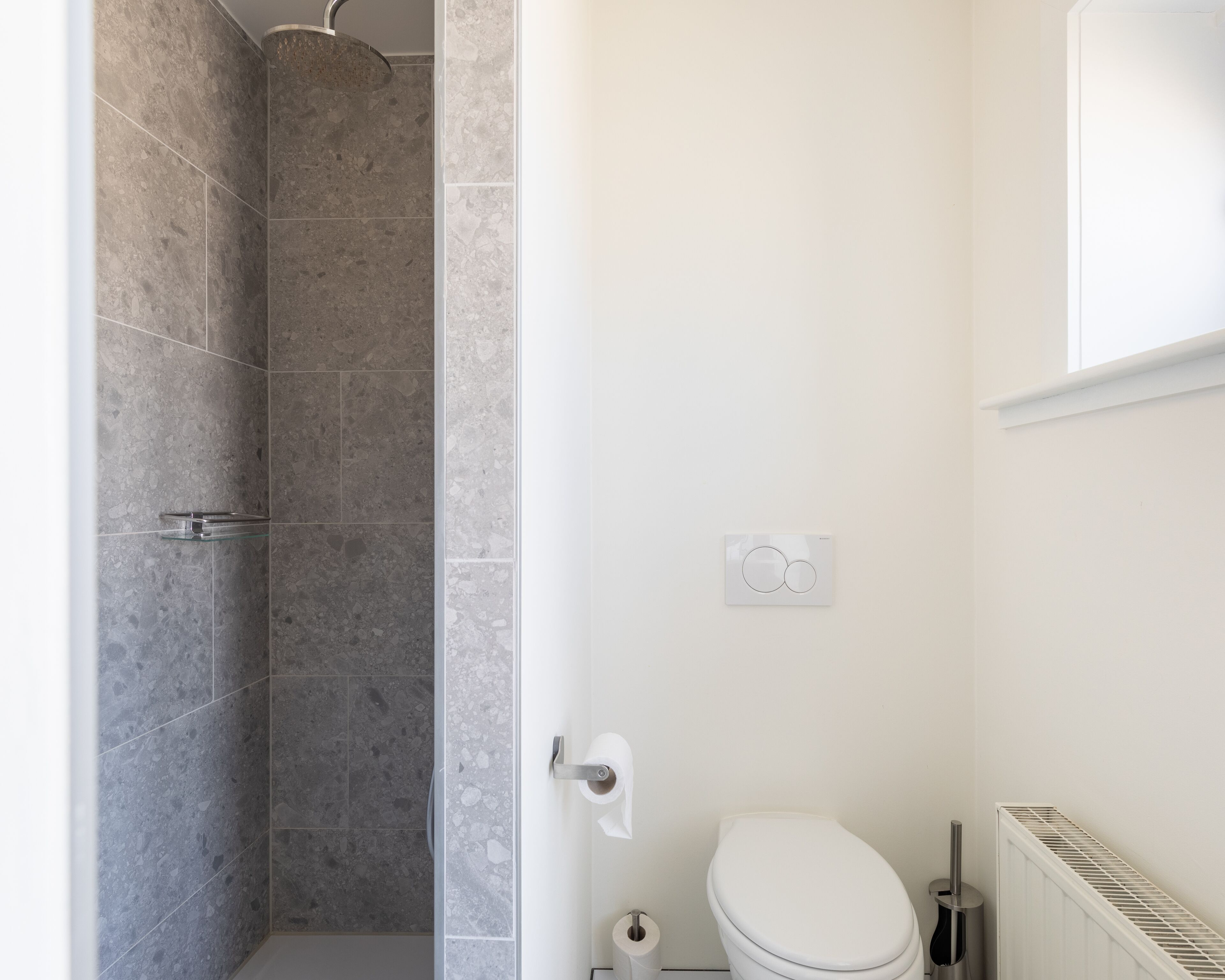 A bathroom with a shower, toilet, and a radiator.