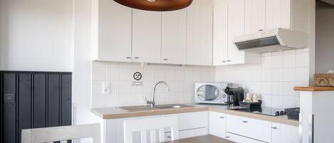 A modern kitchen with white cabinets, a wooden dining table, and a black pendant light.