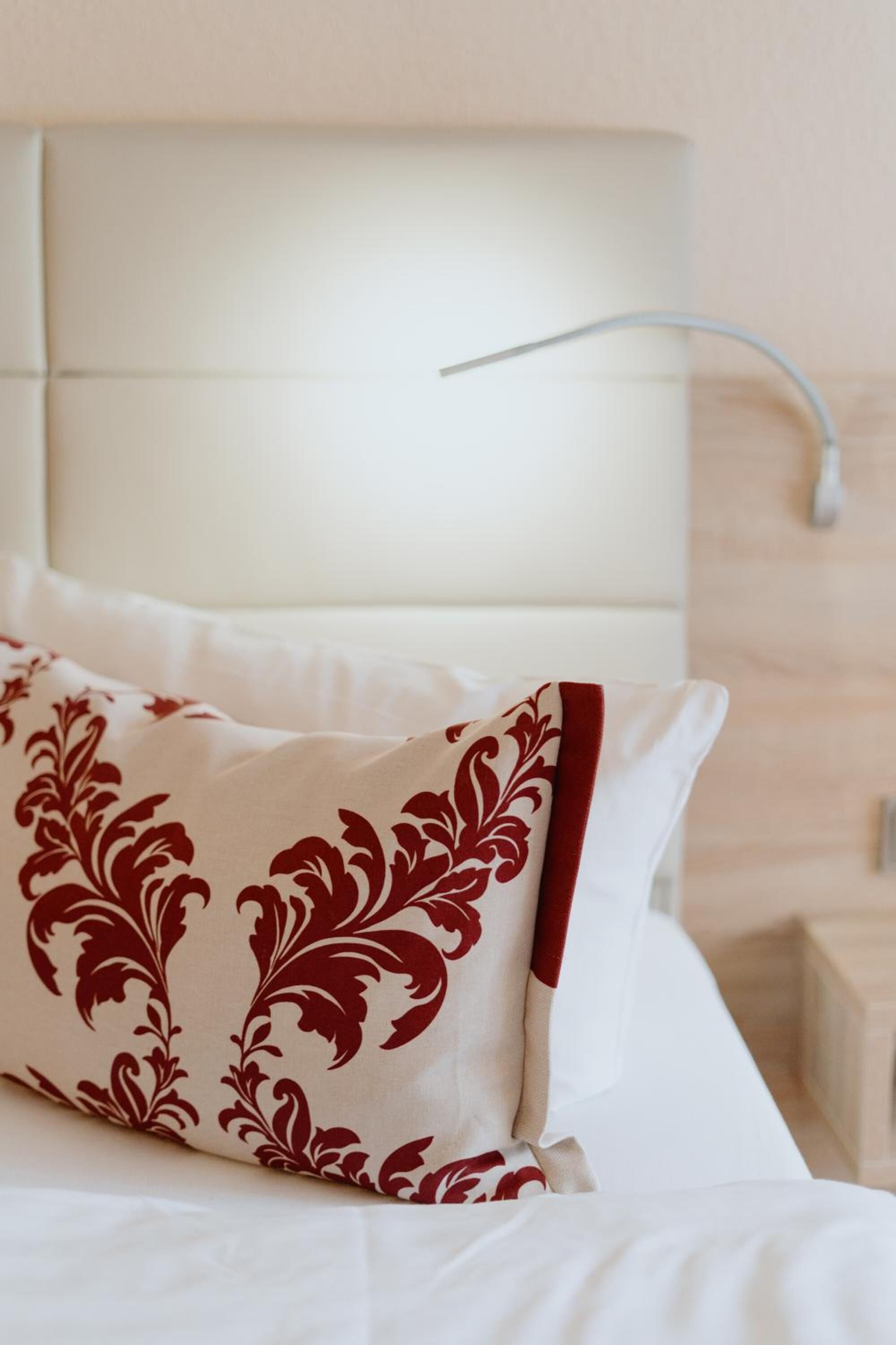 Un lit bien fait, avec une literie blanche et un coussin décoratif à motifs rouges et blancs.