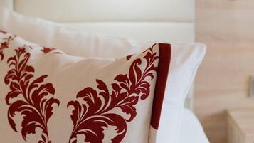 Un lit bien fait, avec une literie blanche et un coussin décoratif à motifs rouges et blancs.