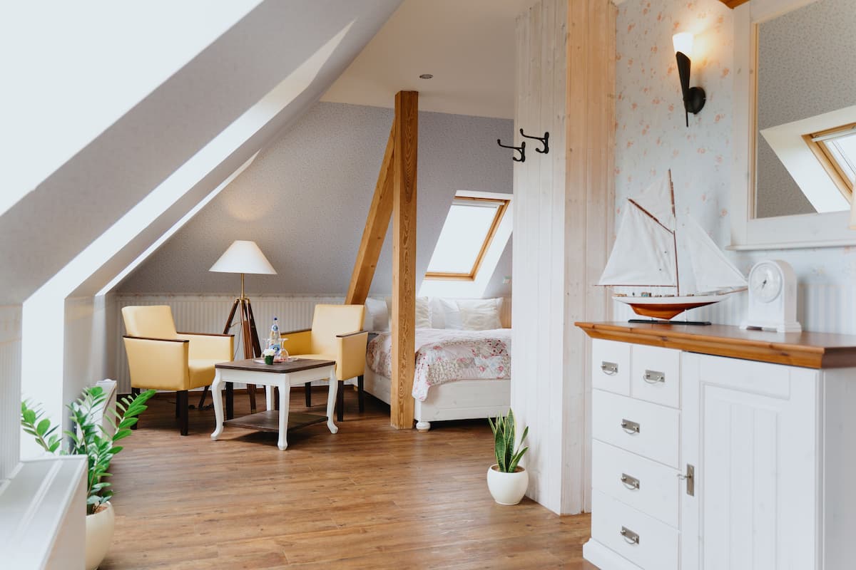 Un acogedor dormitorio tipo loft con techo inclinado, una cama, un escritorio y una silla. Hay una planta en maceta y una pequeña decoración con forma de velero sobre un mueble.