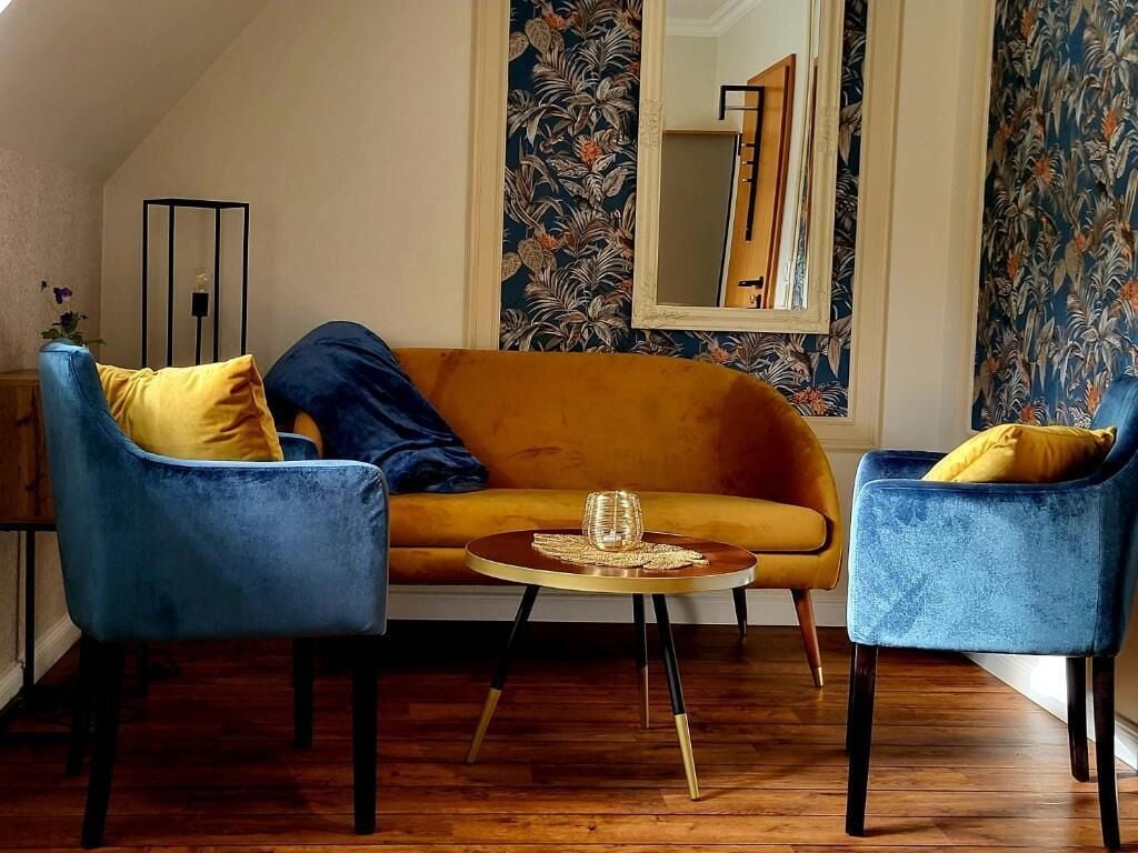 Una habitación con sofá, dos sillones, una mesita redonda y un espejo en la pared.