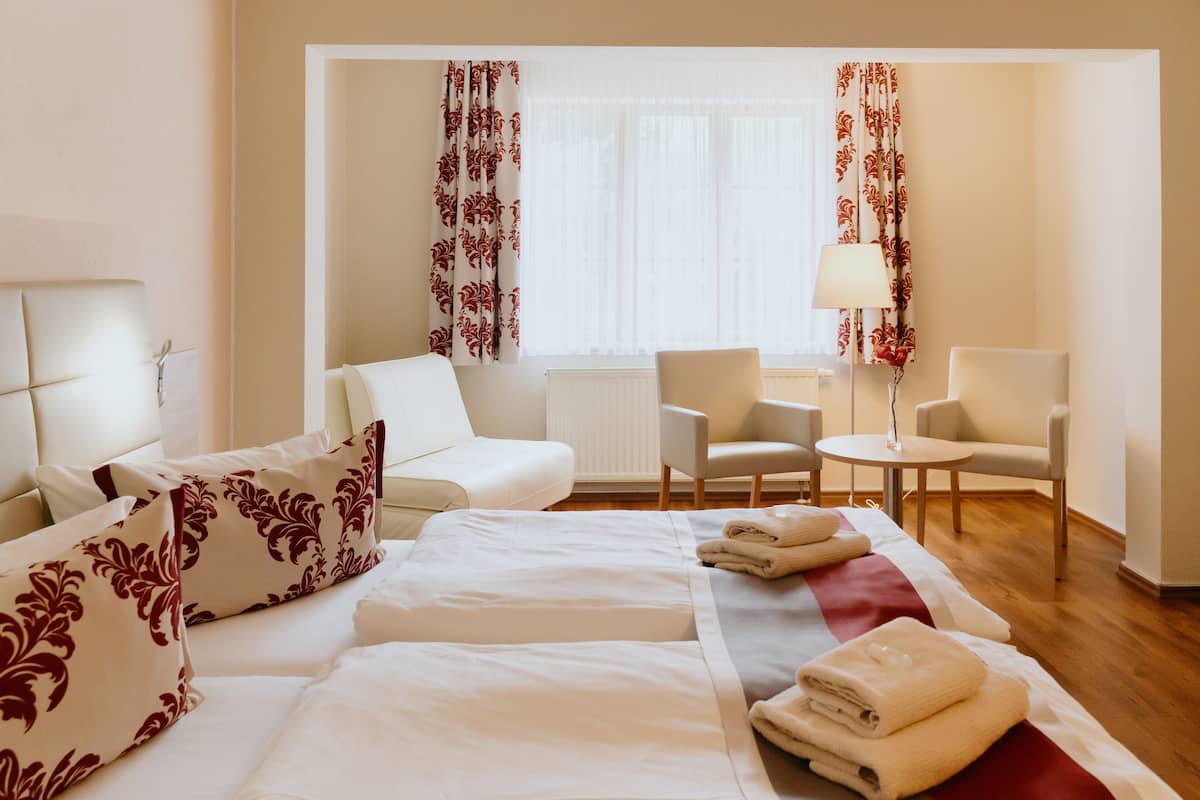 Una habitación de hotel con una cama, dos sillas, una mesita y una lámpara.