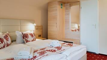 Quarto de hotel com duas camas, um guarda-roupa de madeira, um espelho e um tapete vermelho.