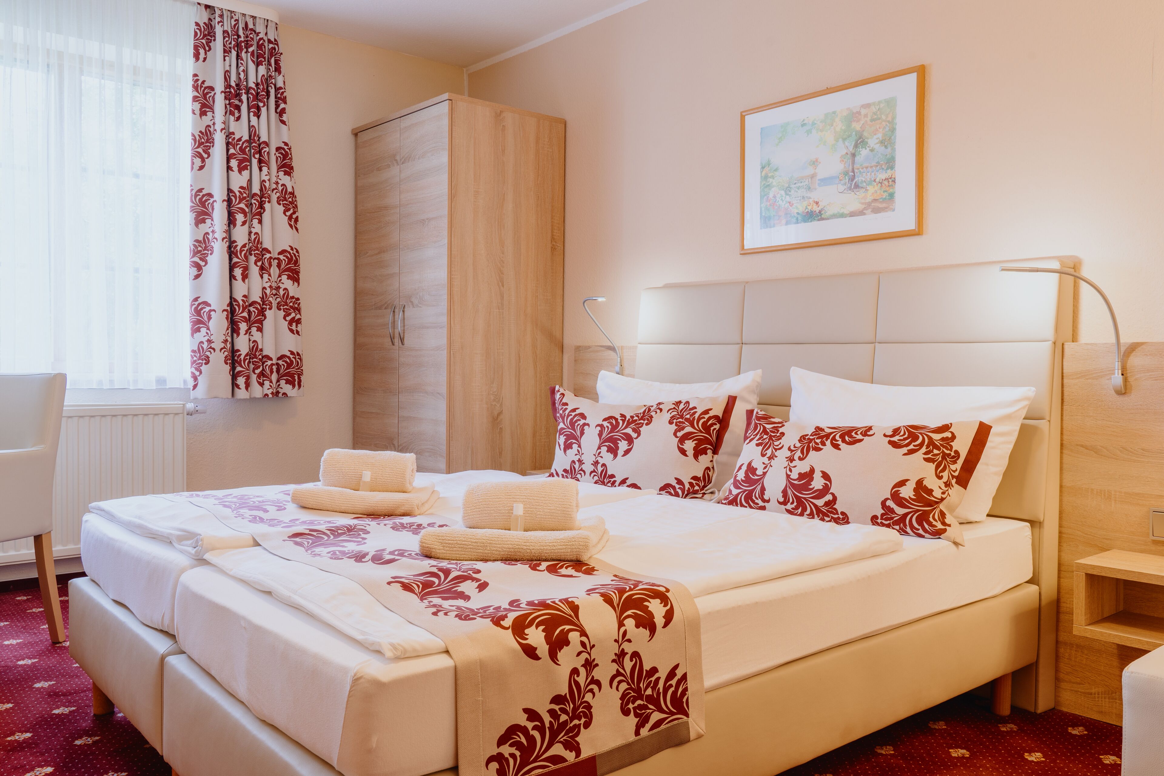 A neatly made bed with a floral bedspread, a wooden wardrobe, and a painting on the wall.