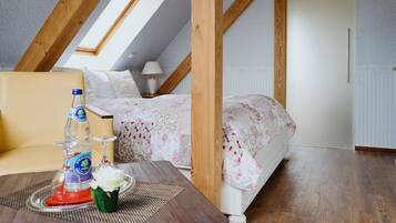 Een slaapkamer met een schuine kap, een bed met bloemenbedrukte lakens, een nachtkastje met een fles en glazen, en een raam met uitzicht op de lucht.