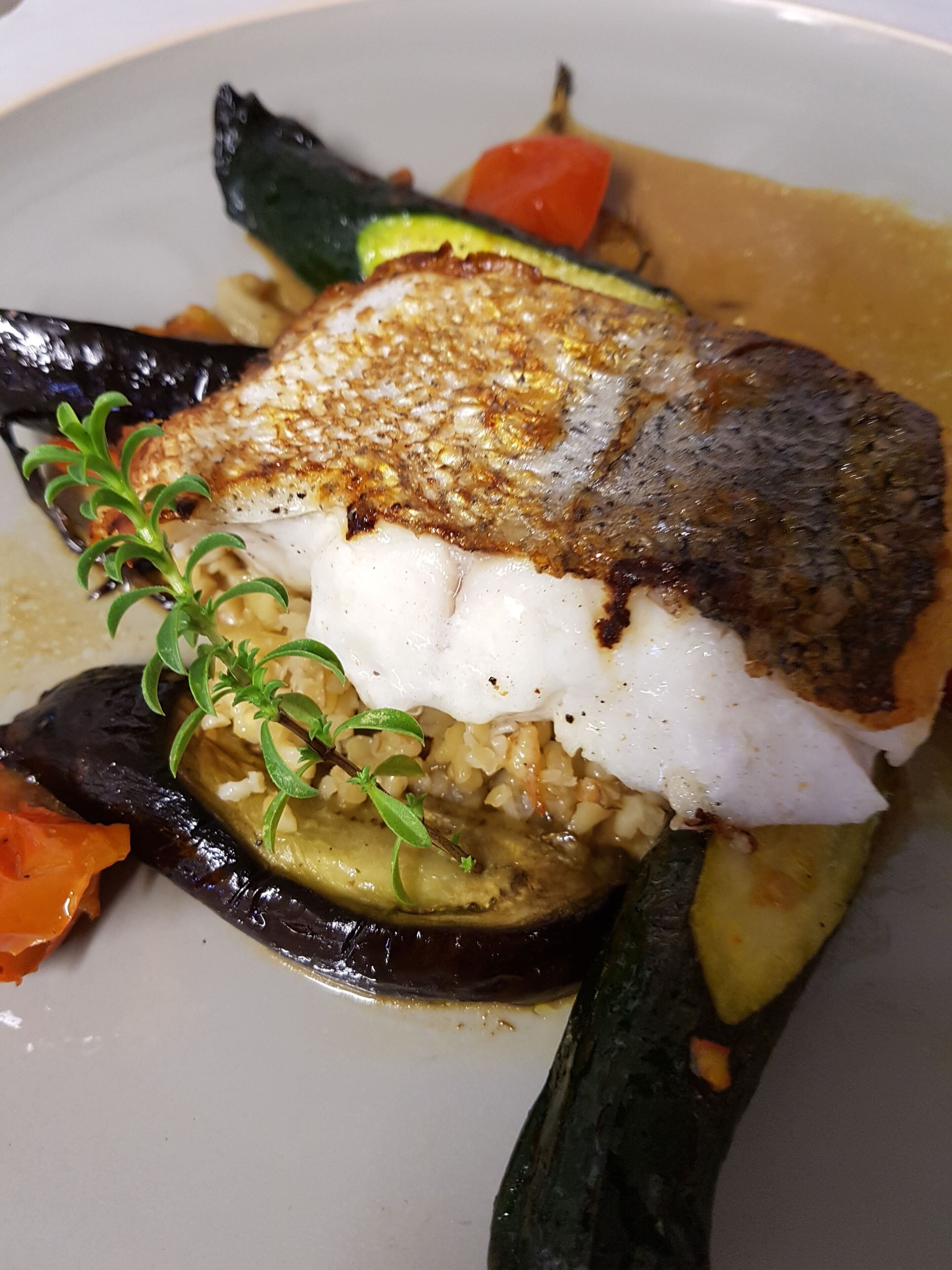 A plate of food with a piece of fish, vegetables, and a garnish.