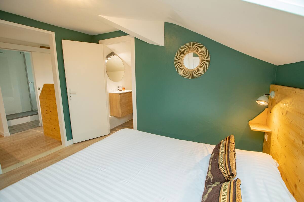 A bedroom with a large bed, a wooden headboard, a wall-mounted mirror, and a wooden door leading to a bathroom.