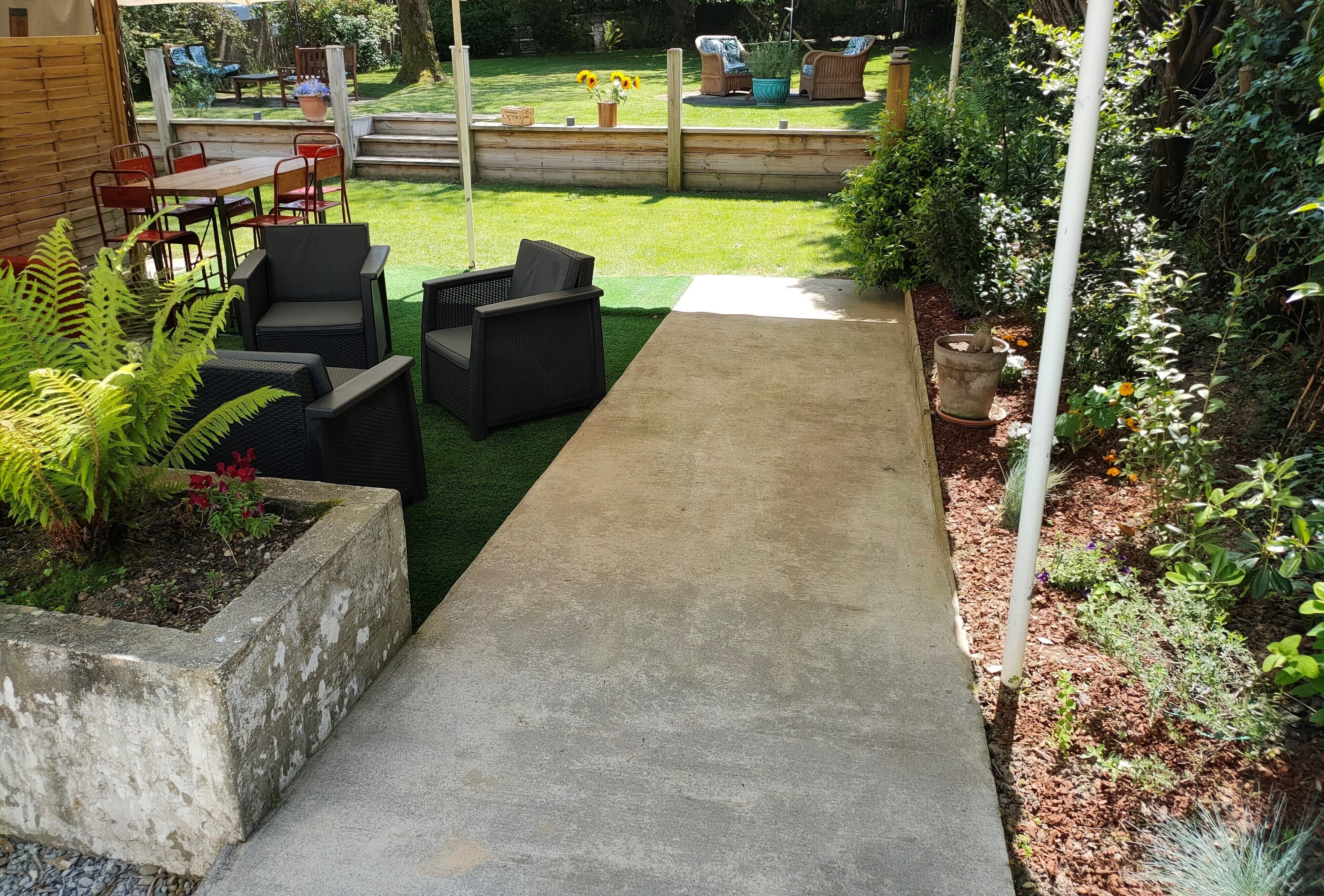 Uma passagem de concreto leva a um pátio com mobiliário de exterior e um jardim.