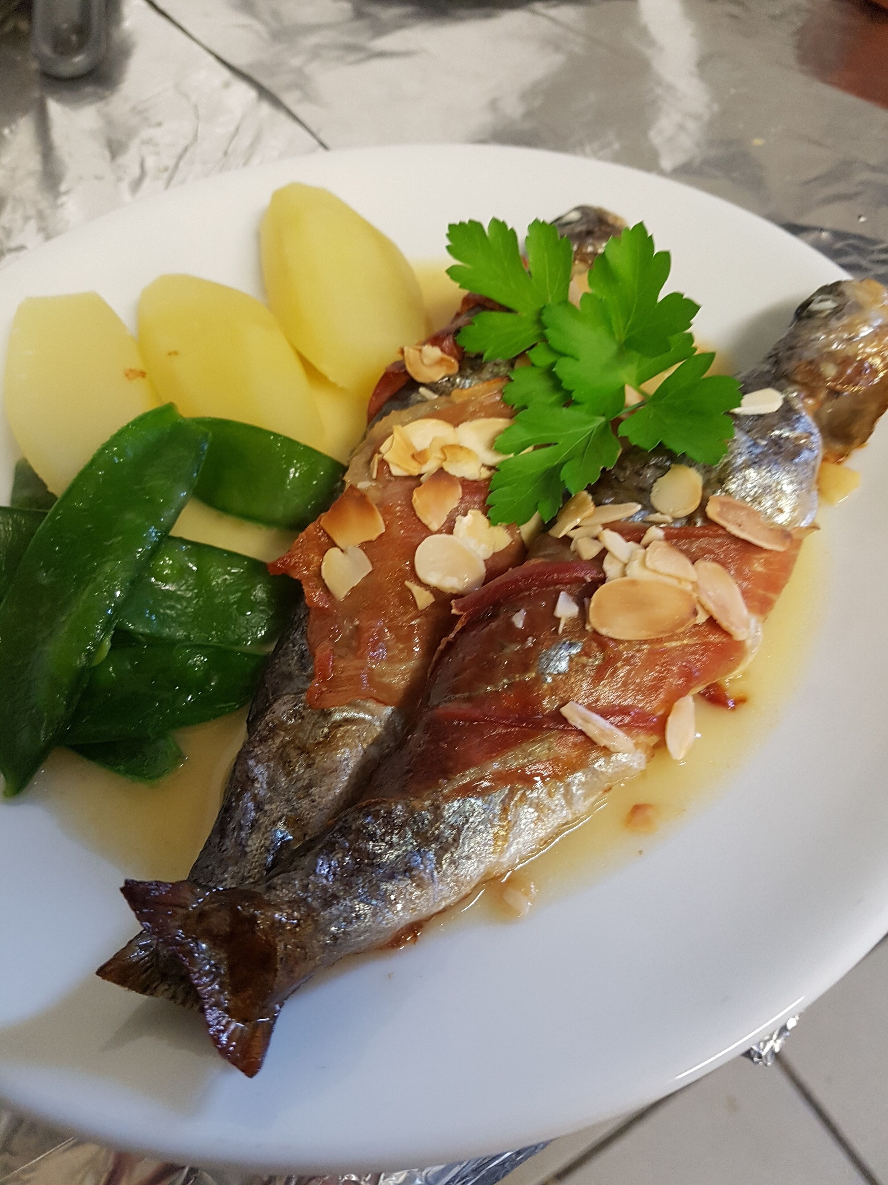 Un plato con pescado, patatas y verduras de hoja verde.