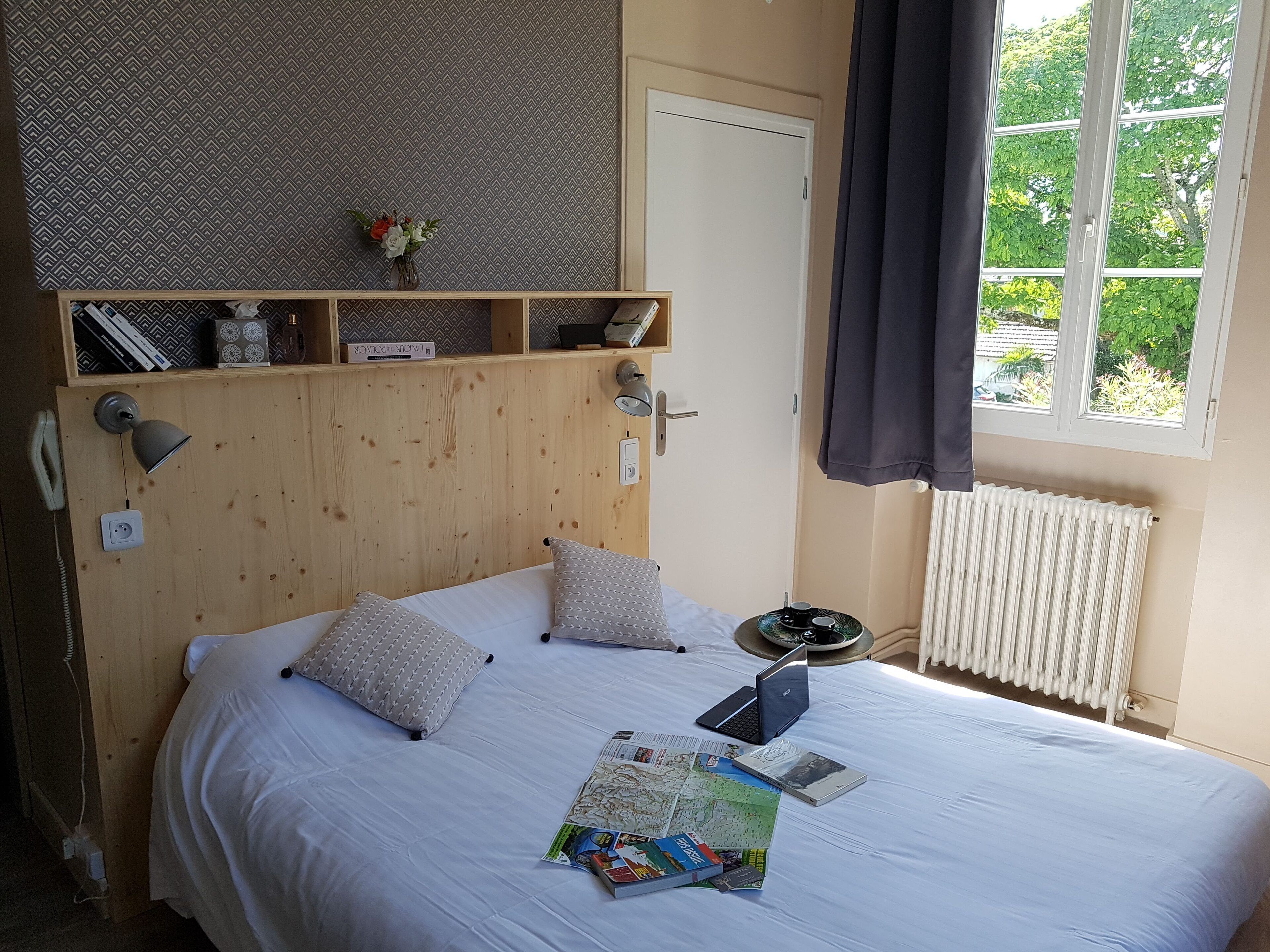A neatly made bed with pillows, a bedside lamp, and a laptop on a wooden headboard.