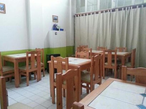 A room with wooden tables and chairs, a whiteboard, and a window with curtains.