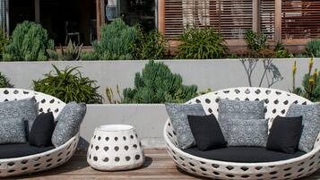 Two wicker sofas with patterned cushions, a round metal table, and a wooden deck with a built-in bench.