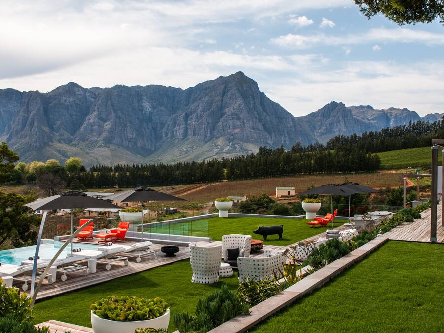 A pool area with lounge chairs and umbrellas, surrounded by a well-maintained lawn and a view of mountains.
