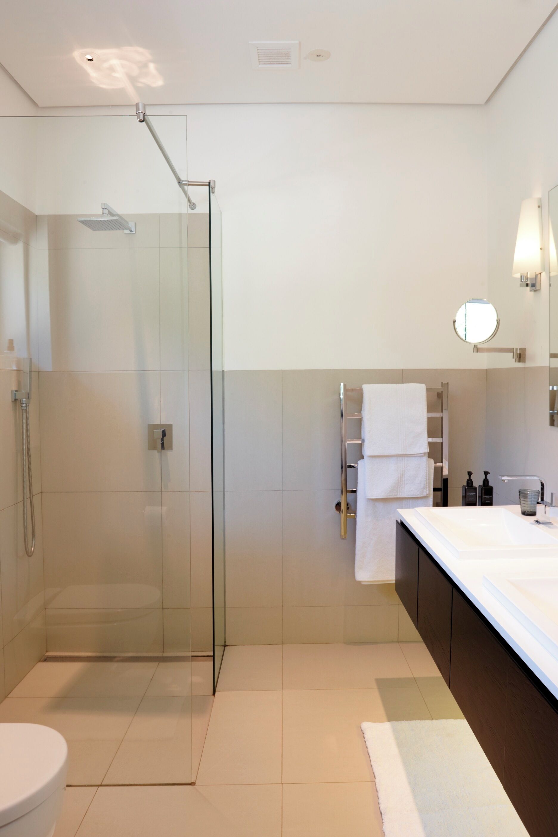 Une salle de bain moderne avec une douche à parois de verre, un lavabo blanc et un miroir doté d’un éclairage circulaire.
