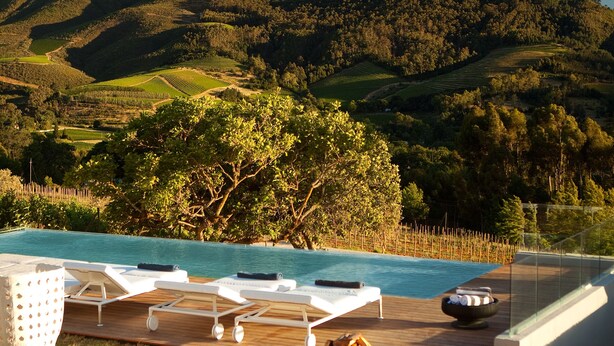 A poolside area with lounge chairs and a hot tub, overlooking a mountainous landscape. - Clouds Estate (Stellenbosch)