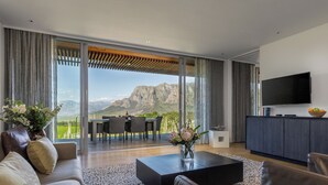 A modern living room with a large sliding glass door, a flat-screen TV, a dining area, and a kitchen. - Clouds Estate (Stellenbosch)