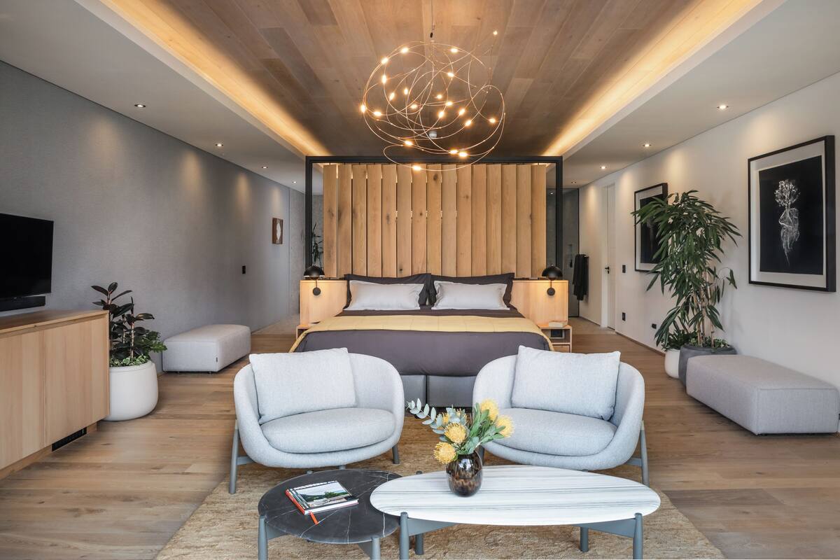 Un dormitorio moderno con una cama grande, dos sillones, una mesita de centro y un televisor.
