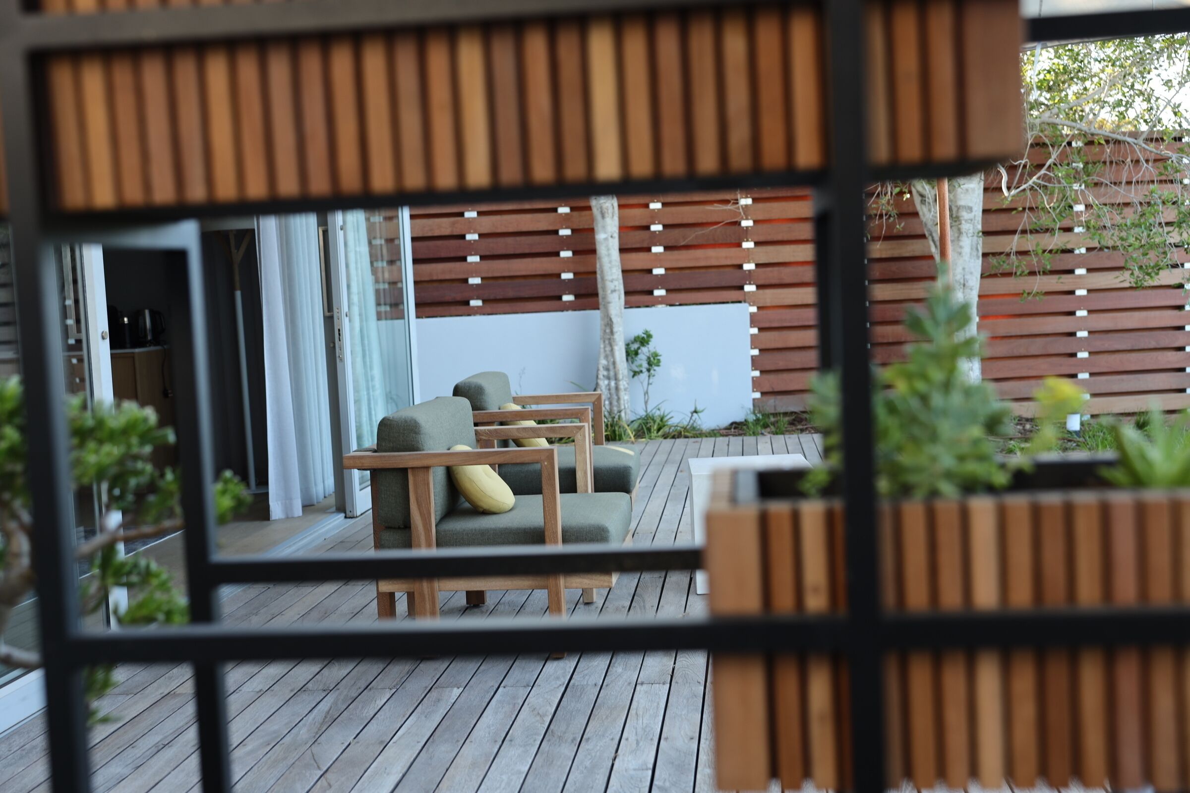 Una terraza de madera con mobiliario exterior, incluyendo un sofá y sillas, y una jardinera con plantas.