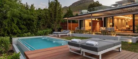 A modern house with a swimming pool, outdoor seating, and a view of the mountains.