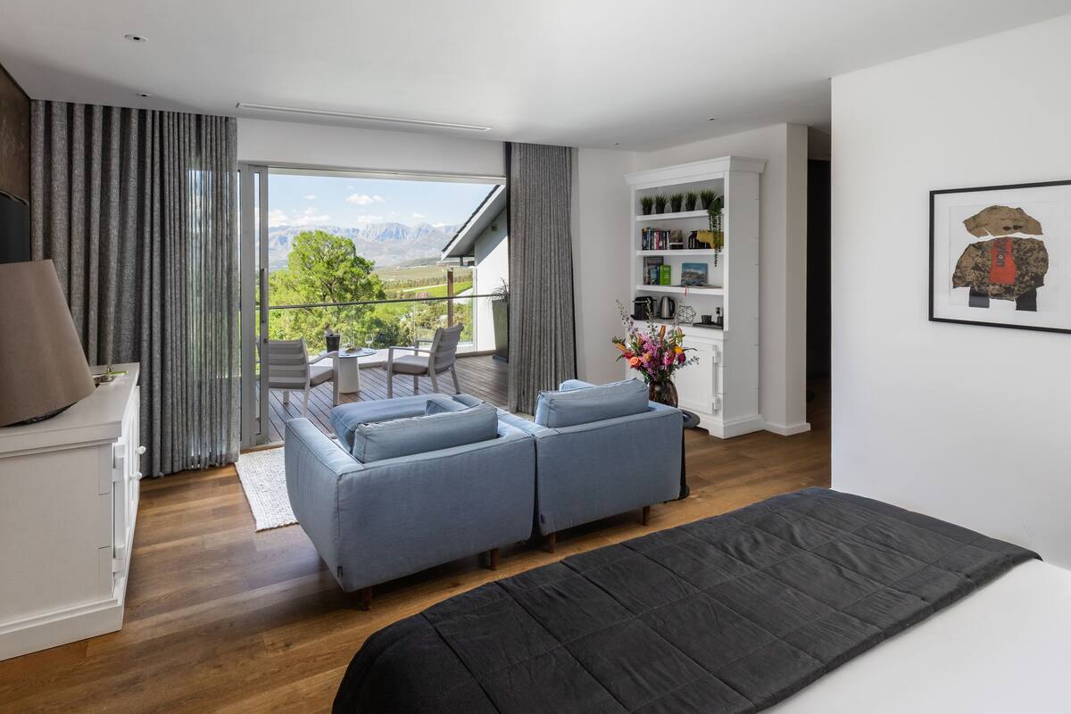 Un dormitorio moderno con una cama grande, un sofá, un balcón con vistas a montañas y una estantería.