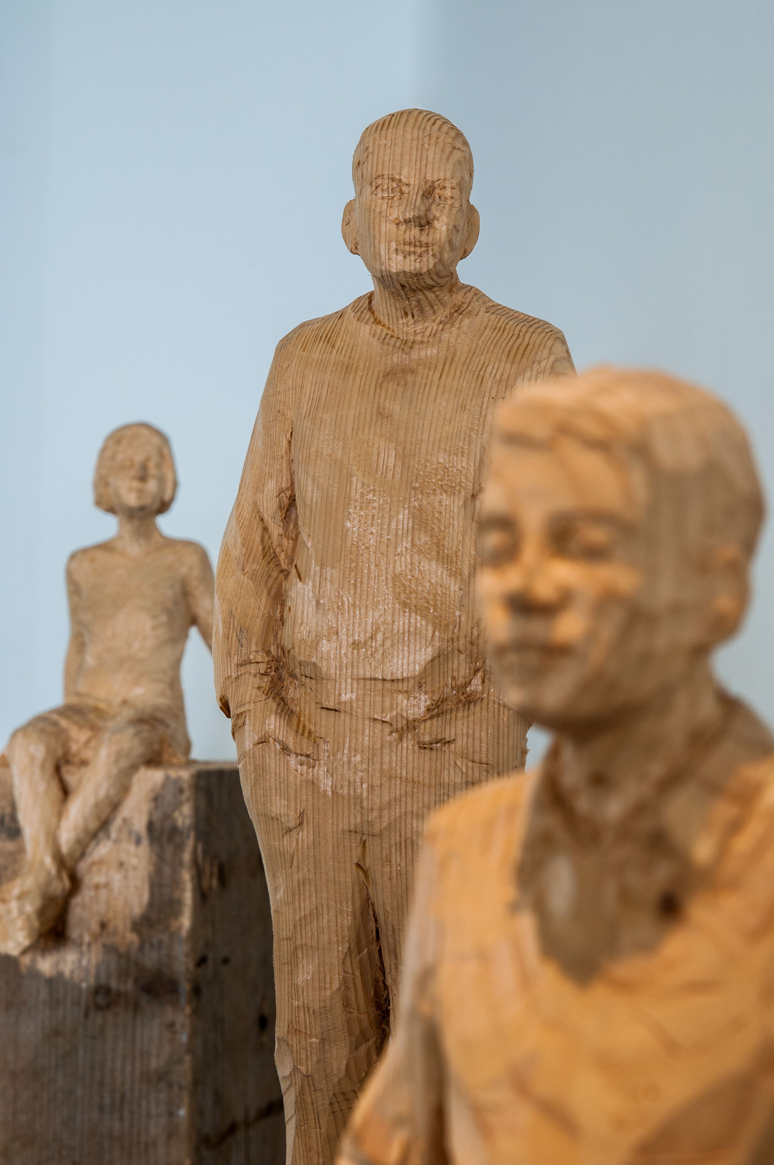 Uma escultura com uma figura sentada, uma figura em pé e uma figura parcialmente visível.
