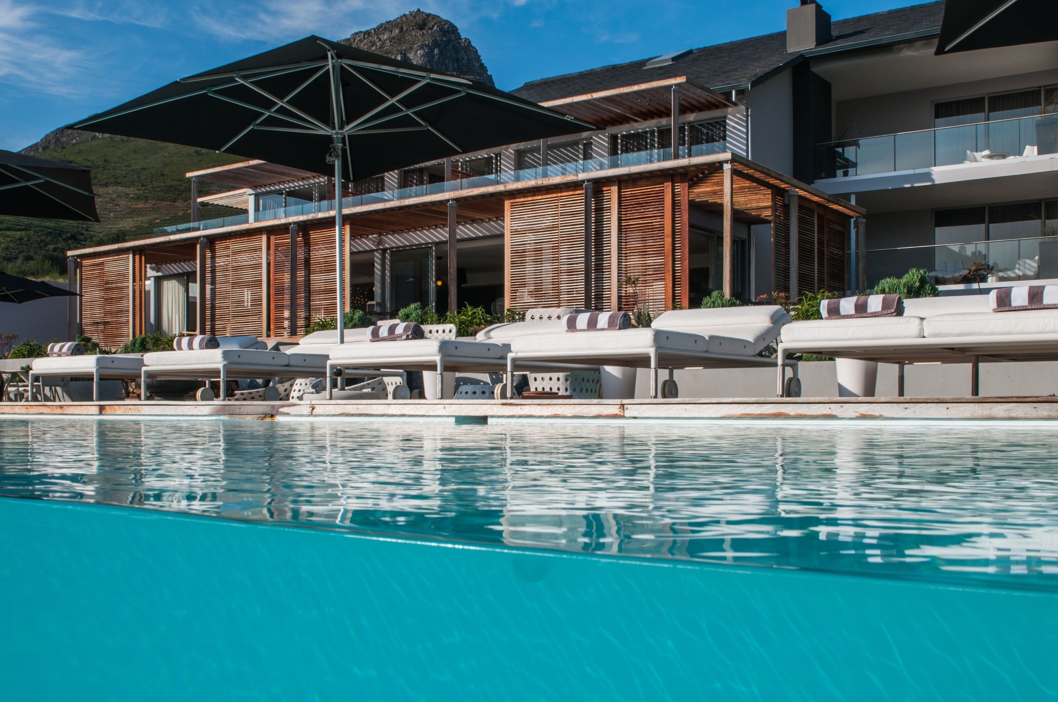 A modern hotel with a pool, outdoor seating, and a mountain view.