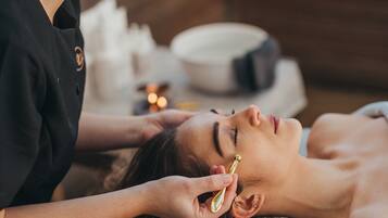 A person receiving a facial treatment in a spa setting with a wooden interior and a bowl of candles in the background.
