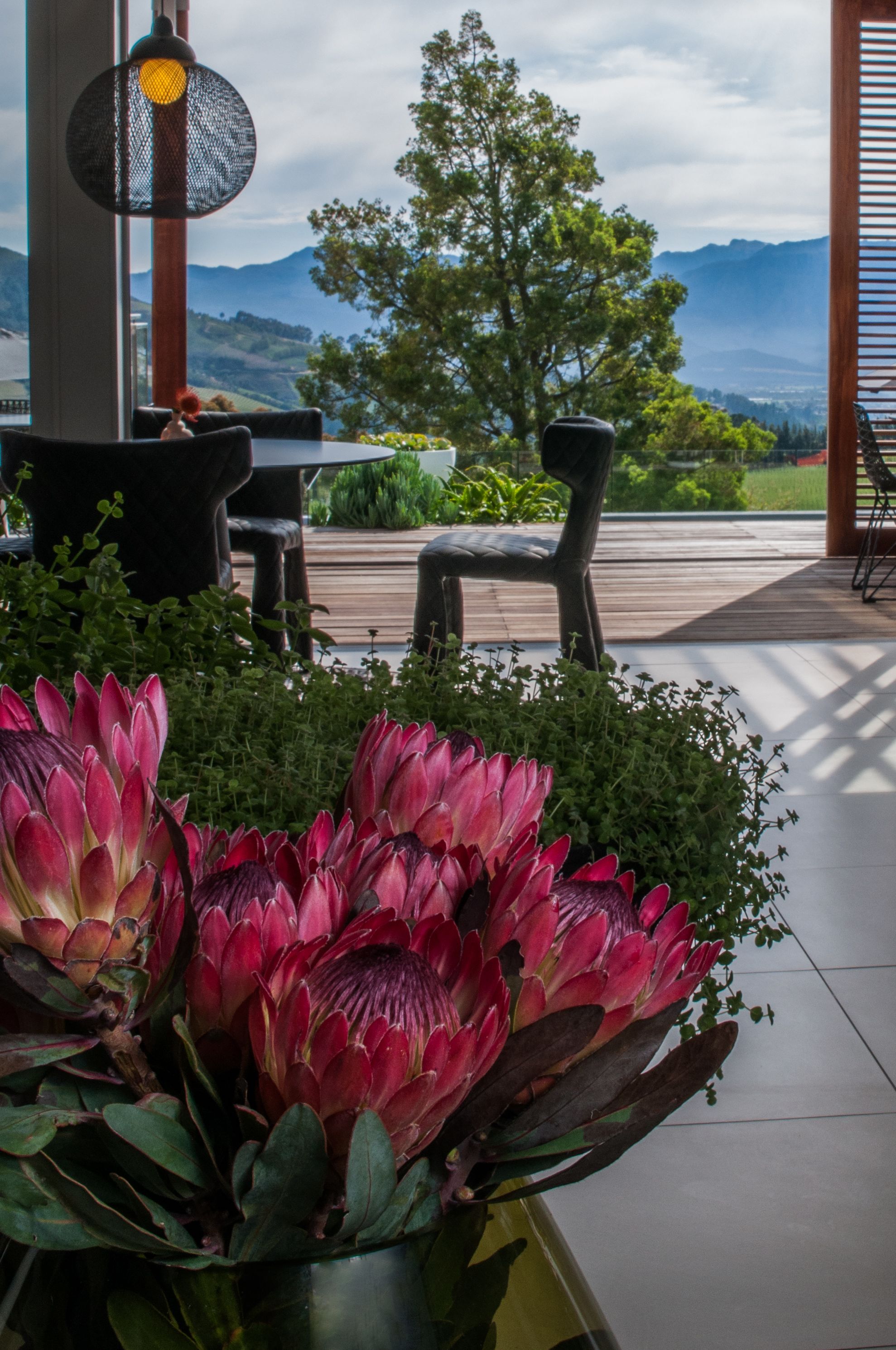 Een patio met uitzicht op bergen, een tafel, stoelen en een grote bloemstuk.