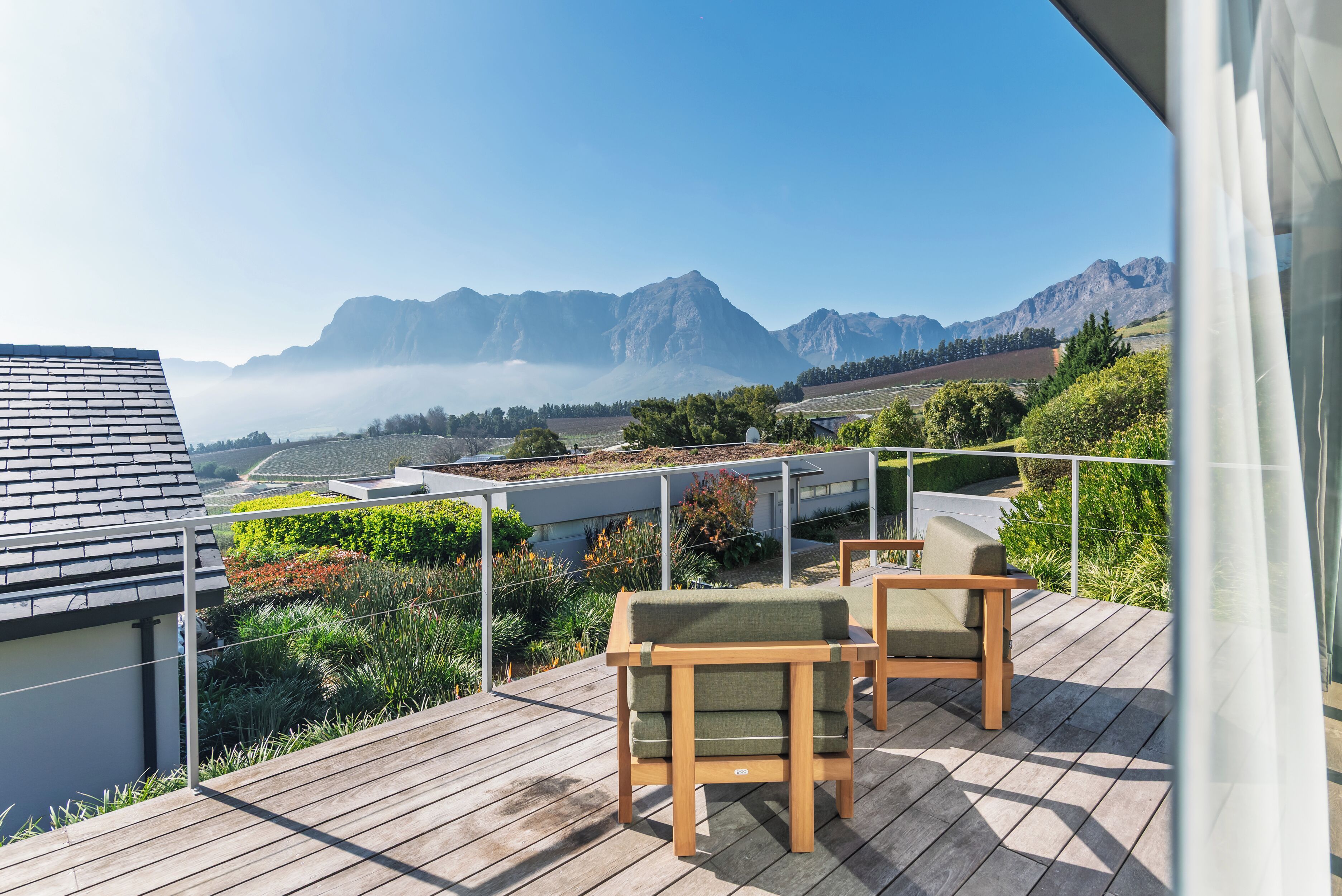 A wooden deck with outdoor furniture, overlooking a mountainous landscape with a clear sky.